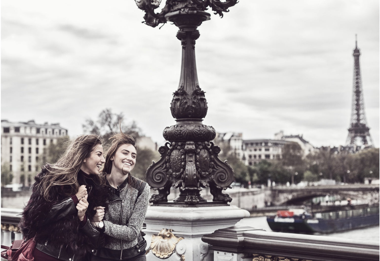2 chicas elegantes que están en un puente cruzando el sena en Paris. En el fondo, se ve la Torre Eiffel