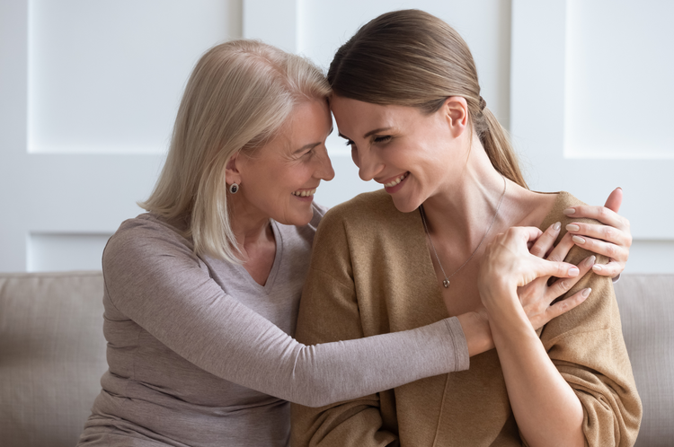una madre enlaza a su hija adulta, sonriendo, felices de estar juntas, gran complicidad entre ellas.