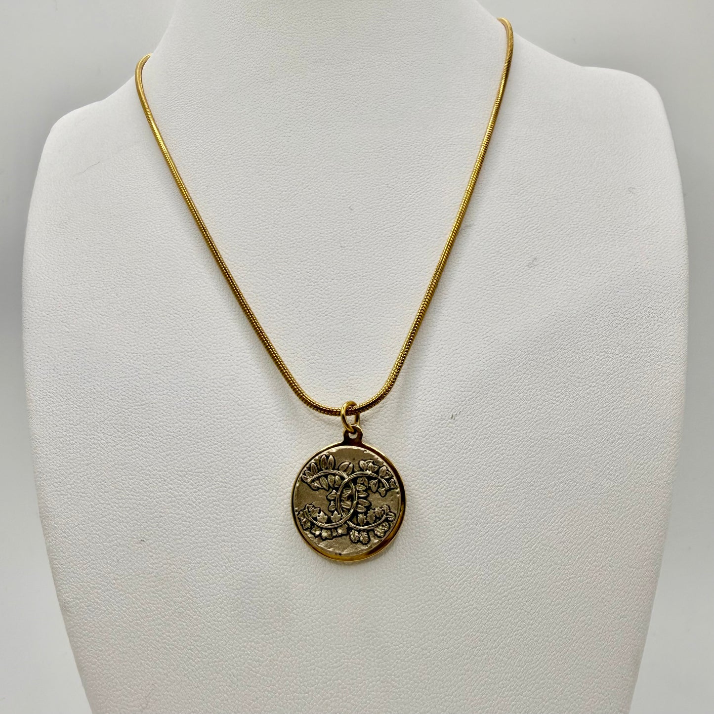 Joya artesanal sostenible con botón CHANEL recuperado y reciclado en una ropa en desuso.