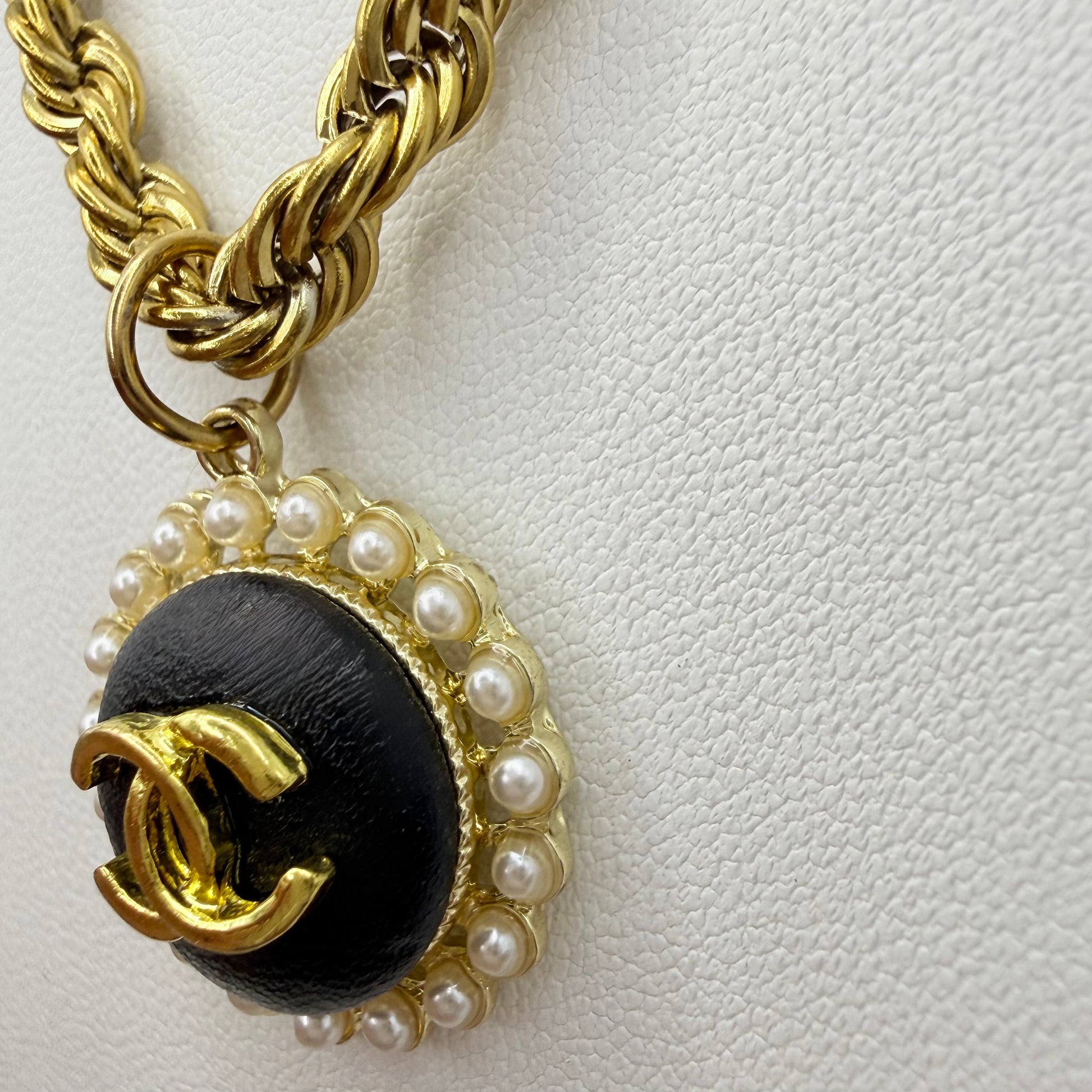 Detalle del botón recuperado de marca de lujo, negro y dorado, en collar artesanal DEMETRA hecho a mano por EOS UPCYCLING